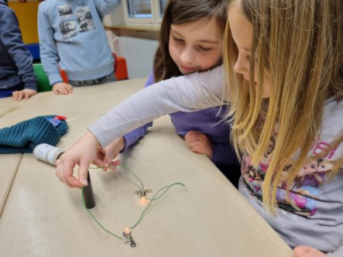 Kinder beim Experimentieren mit Batterienen Lämpchen und Kabeln