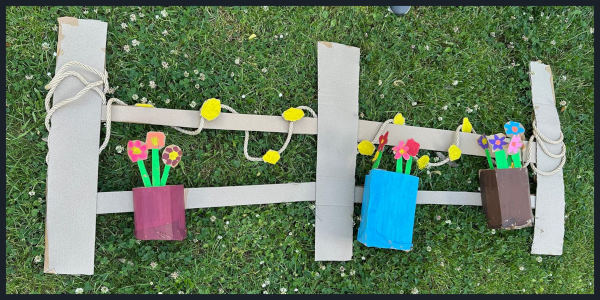 Ein gebastelter Zaun aus Pappe mit gebastelten Blumenkästen