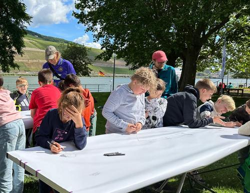 Kinder am Kulturufer am Rhein vor einem Tisch mit einem großen Papierbogen